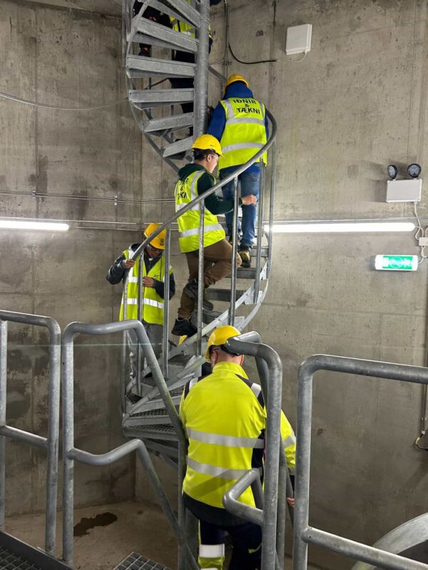 Fjórar manneskjur í vinnugöllum ganga upp brattar vinnutröppur.